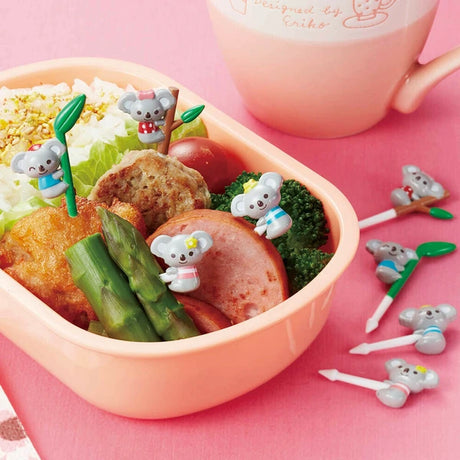 Bento box with food and cute koala-shaped desk accessories on a pink background